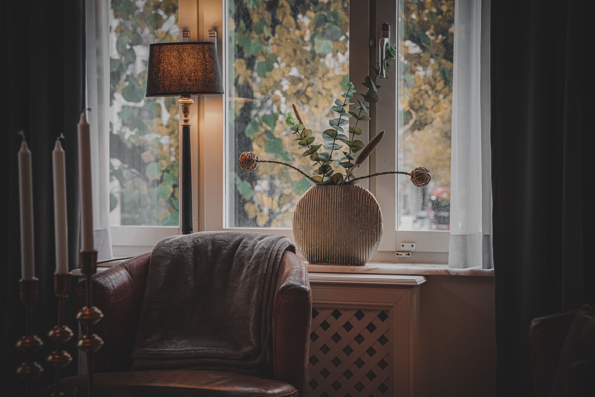 A cozy room with a leather chair, a lamp, and a vase with a plant on a windowsill.