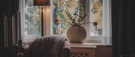 A cozy room with a leather chair, a lamp, and a vase with a plant on a windowsill.