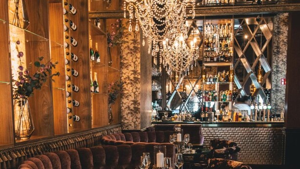 A bar area with a wooden wall displaying bottles, a chandelier, and plush seating. - Mojo Hotell (Örebro)