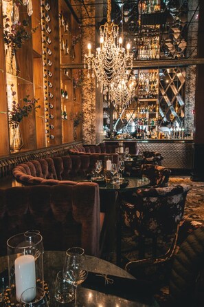 Zona de bar con pared de madera que muestra botellas, una araña y asientos cómodos.