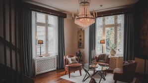 A spacious living room with a chandelier, leather chairs, a glass coffee table, and large windows with curtains. - Mojo Hotell (Örebro)