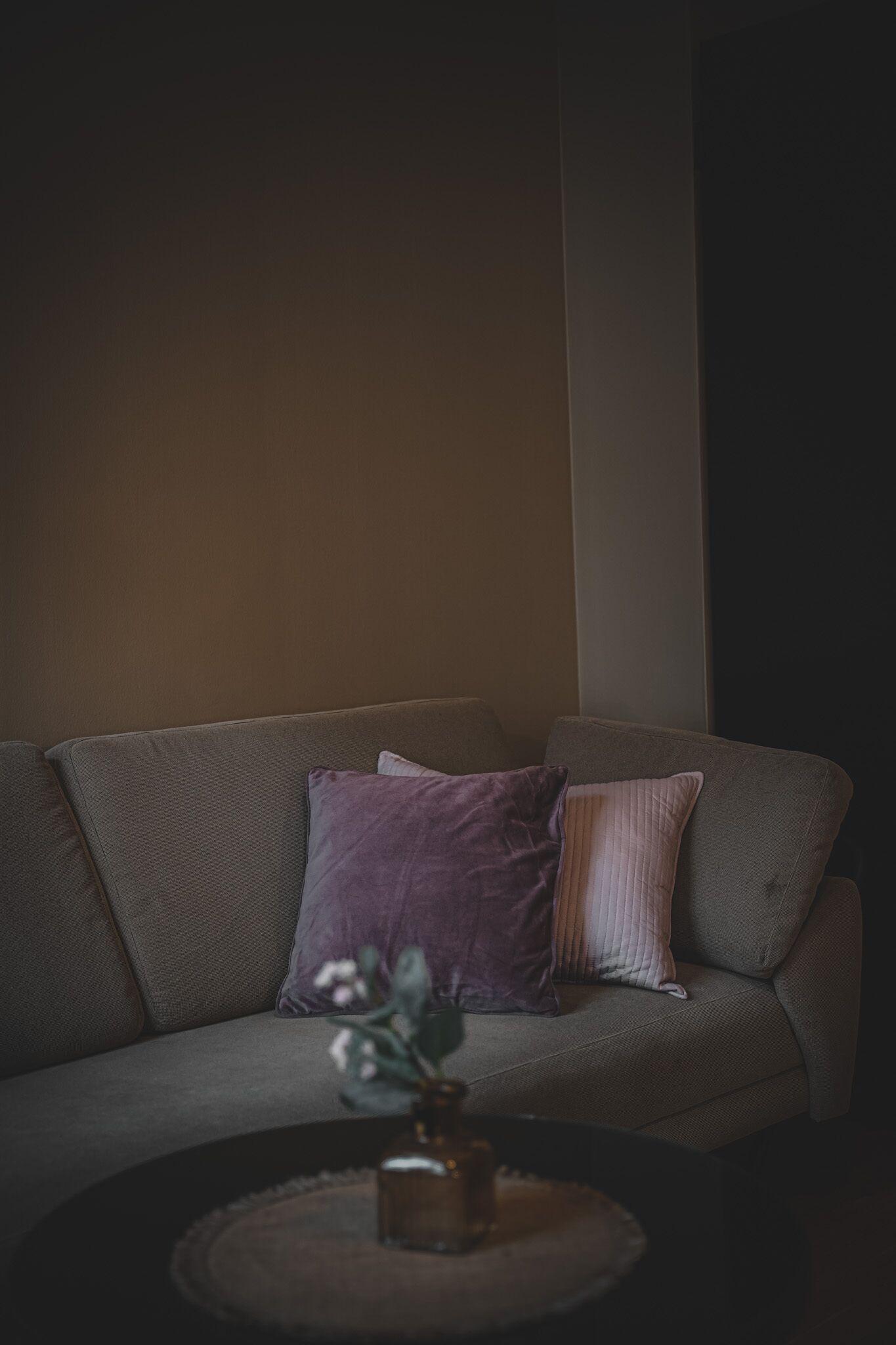 Un sofá con dos almohadas y una mesita con un florero.