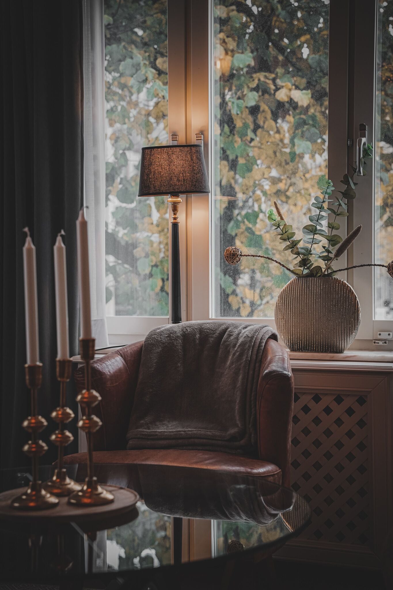 A cozy room with a leather armchair, a lamp, and a vase with greenery.