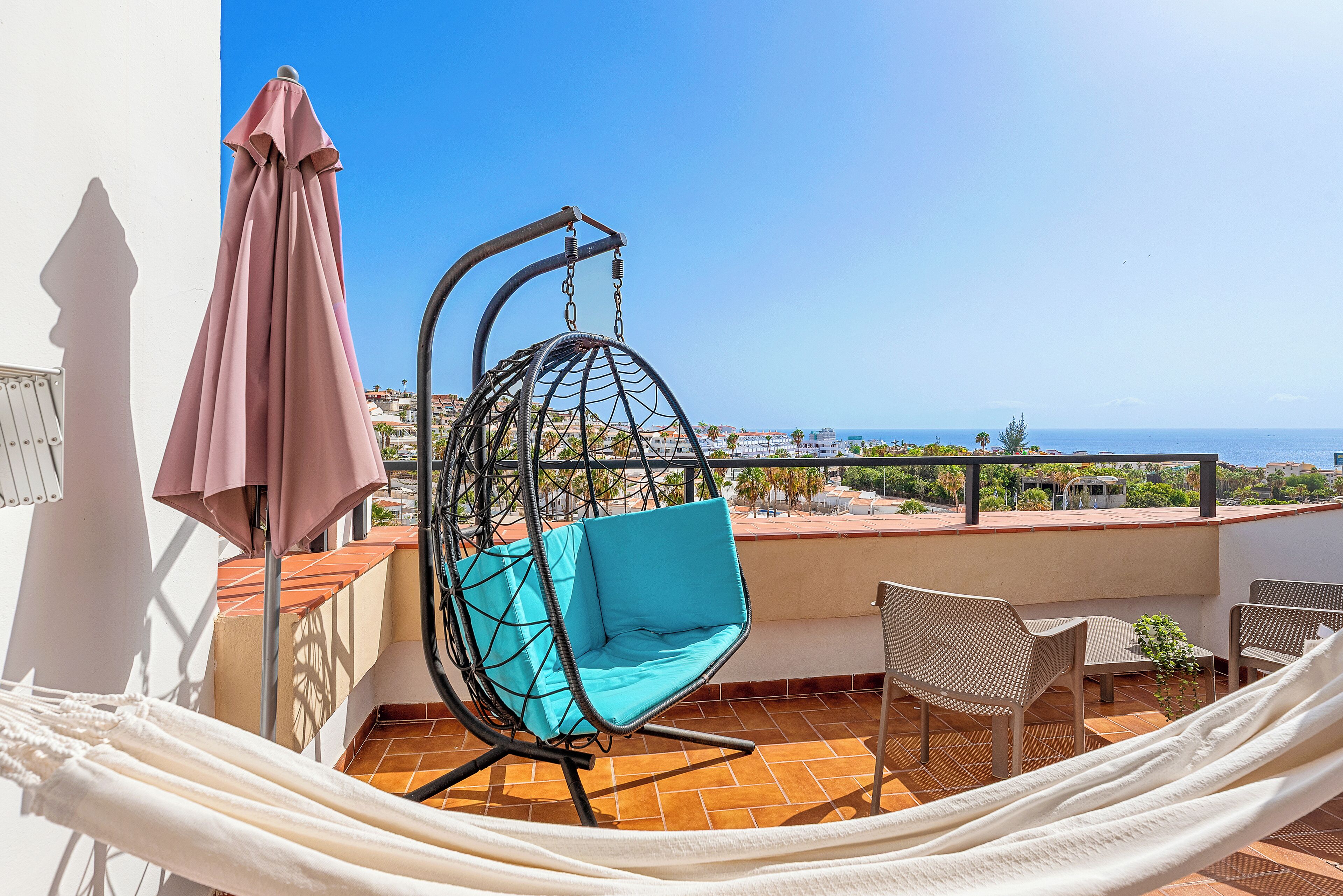 A balcony with a hanging chair, a hammock, and a table with chairs.