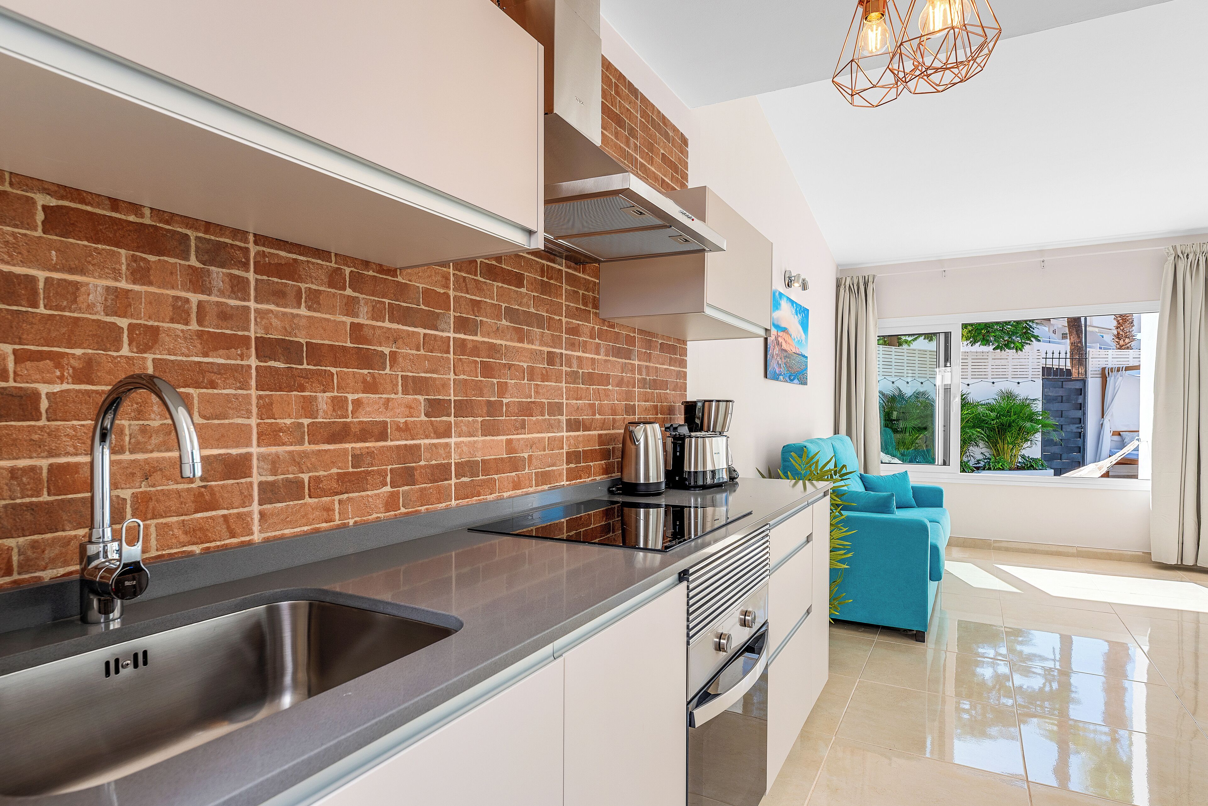 A modern kitchen with a brick backsplash, stainless steel sink, and a coffee maker on the counter.
