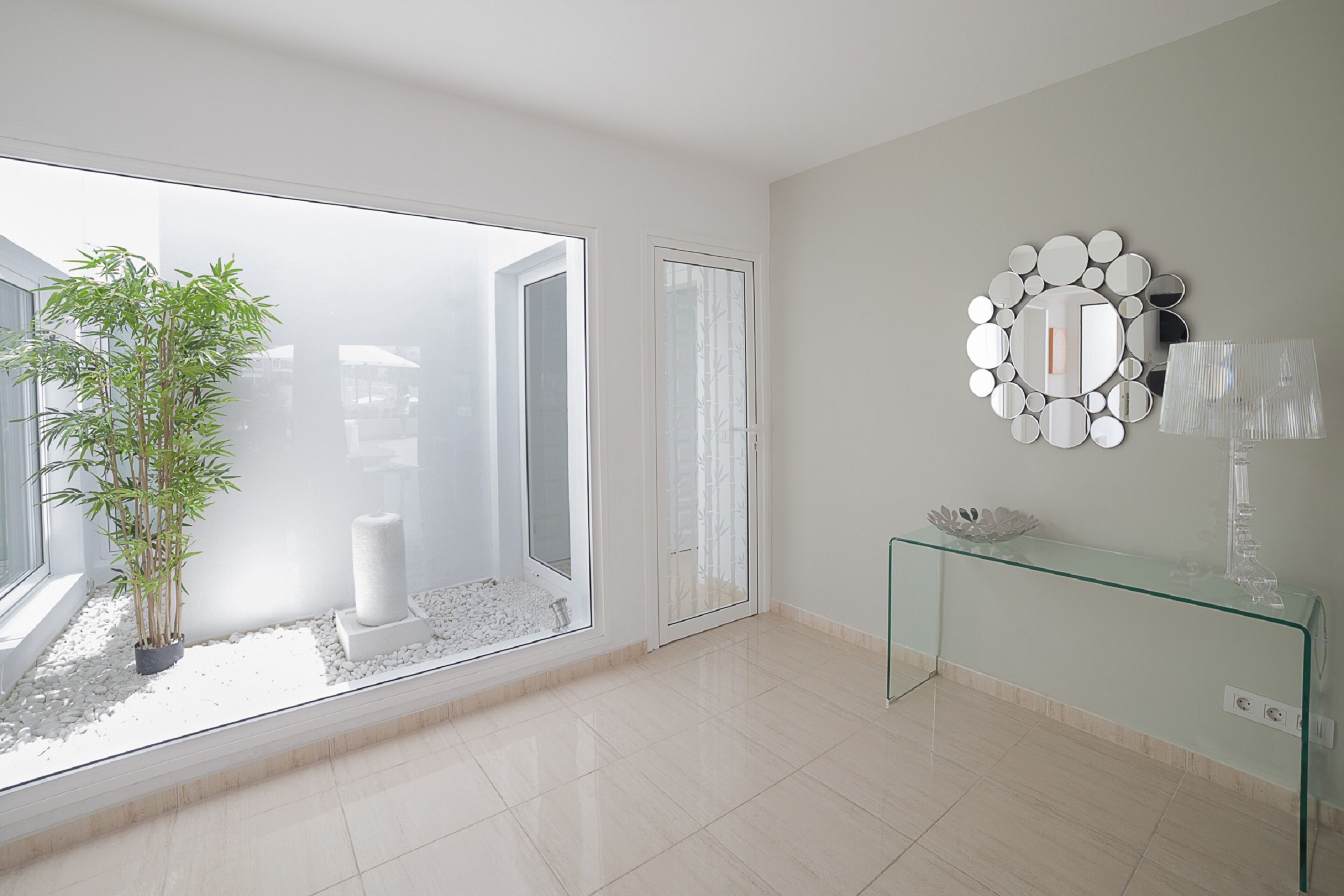 A modern room with a large window, a glass console table, and a decorative mirror on the wall.