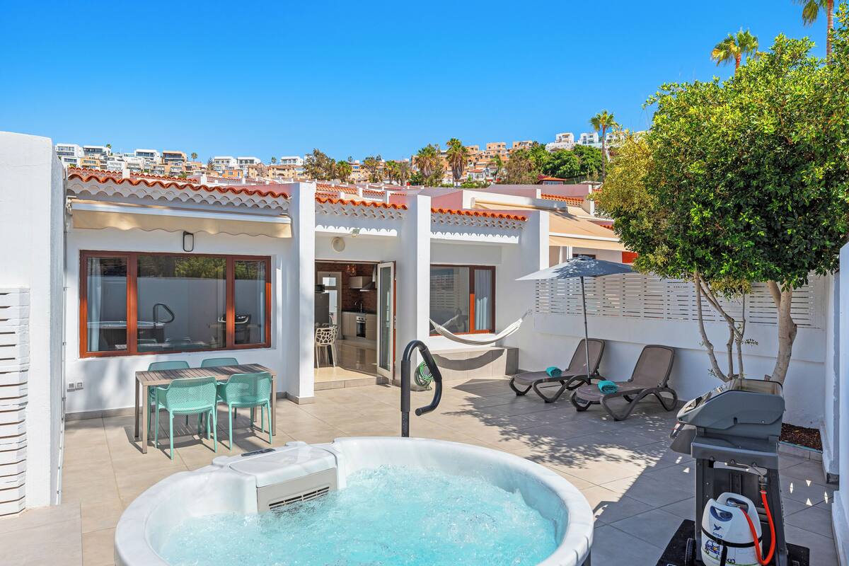 Zona de piscina con hidromasaje, sillas de descanso y una mesa de comedor con sillas.