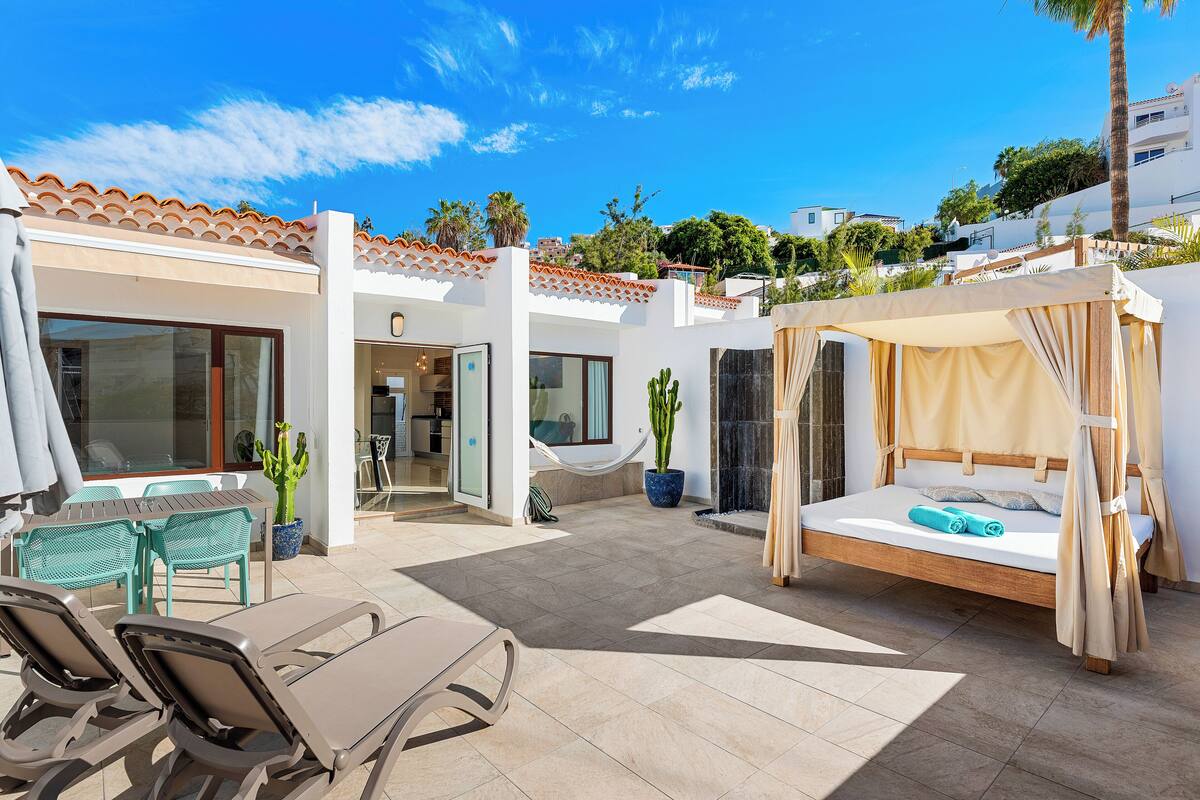 Un patio moderno al aire libre con cama, sillas de descanso y zona de comedor.