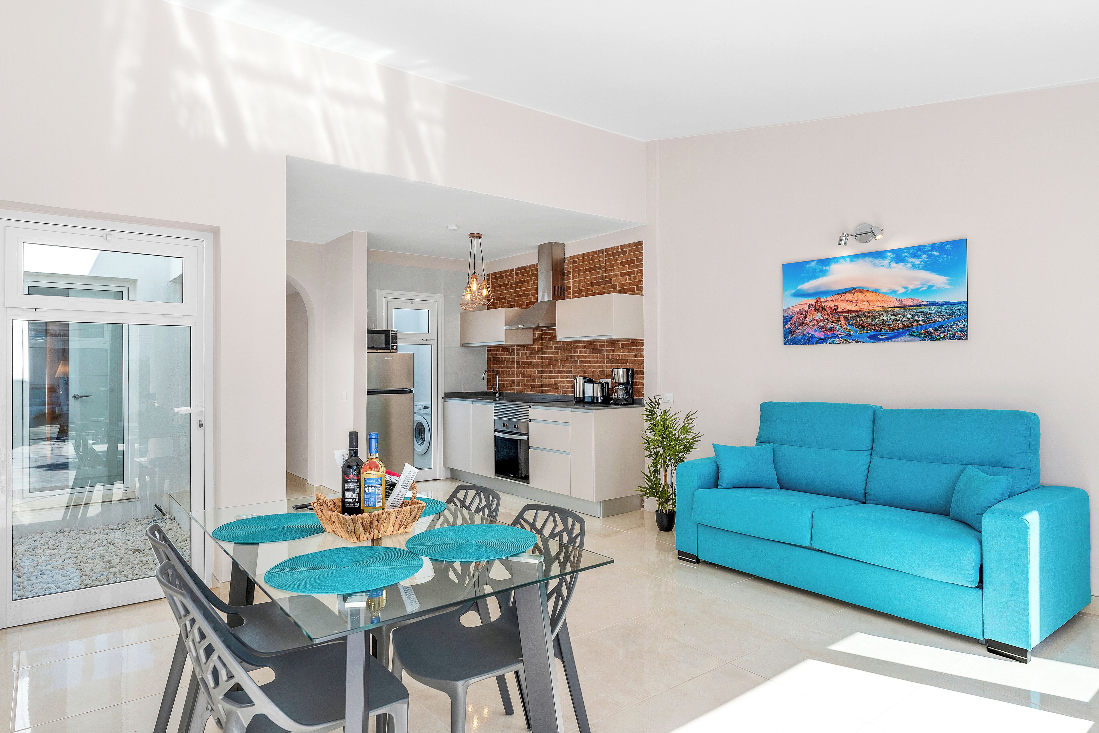 Un salon moderne avec un canapé bleu, une table à manger en verre entourée de chaises, et une cuisine en arrière-plan.