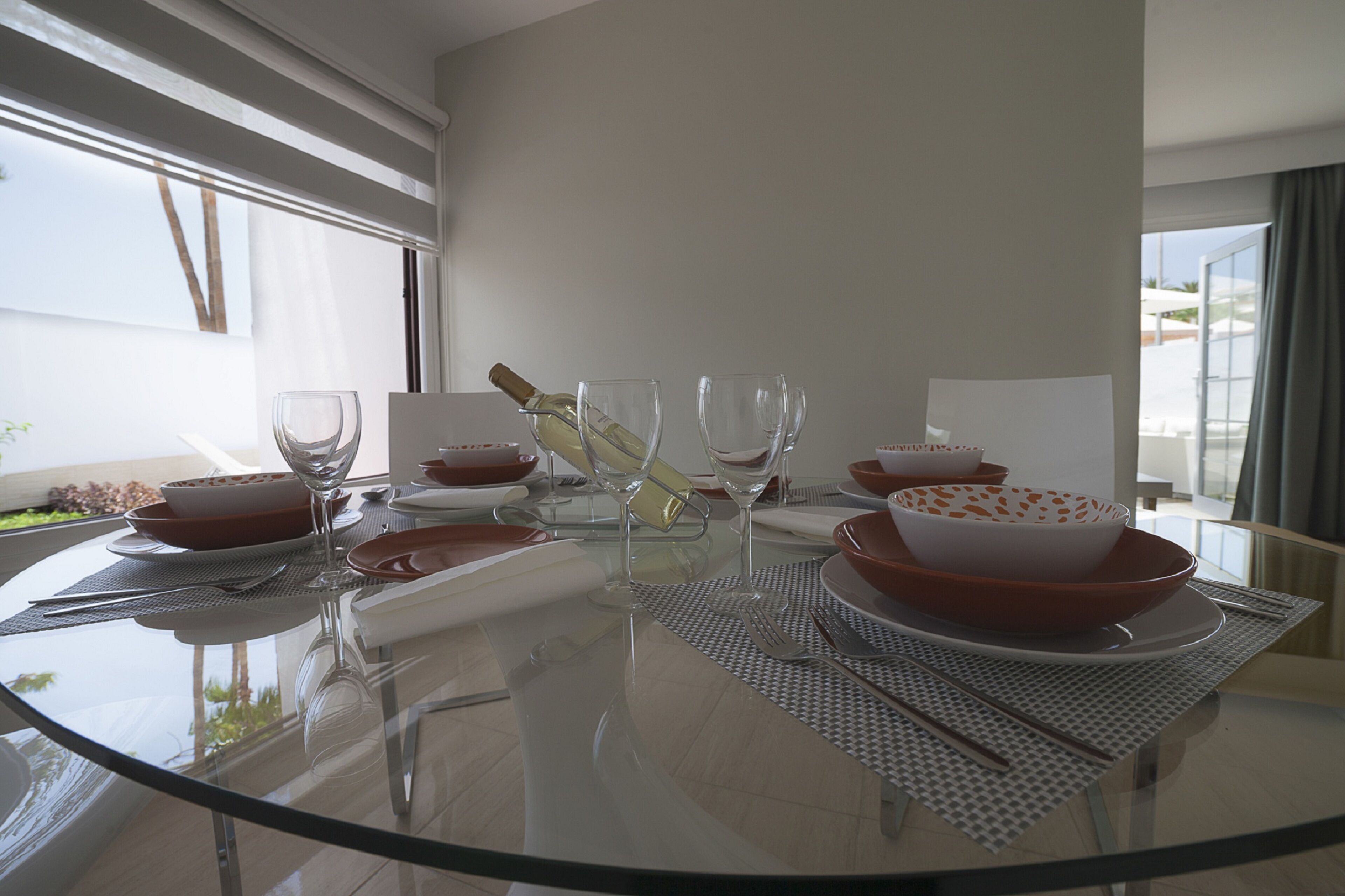 Une table à manger dressée avec des bols rouges et blancs, des verres à vin et une bouteille.