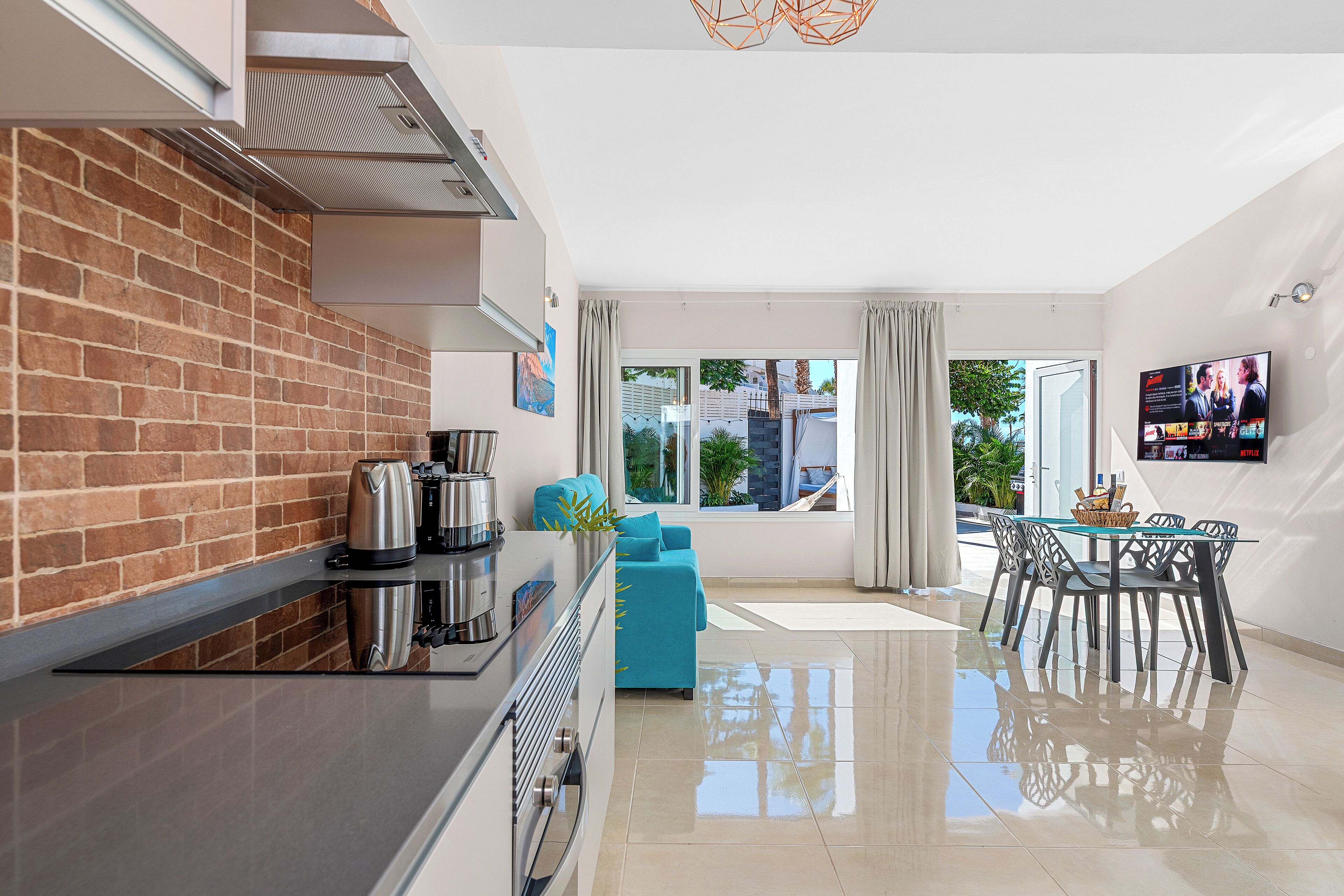 Una cocina moderna con pared de ladrillo, electrodomésticos de acero inoxidable y un comedor con mesa y sillas de vidrio.