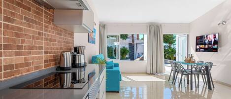 Una cocina moderna con pared de ladrillo, electrodomésticos de acero inoxidable y un comedor con mesa y sillas de vidrio.