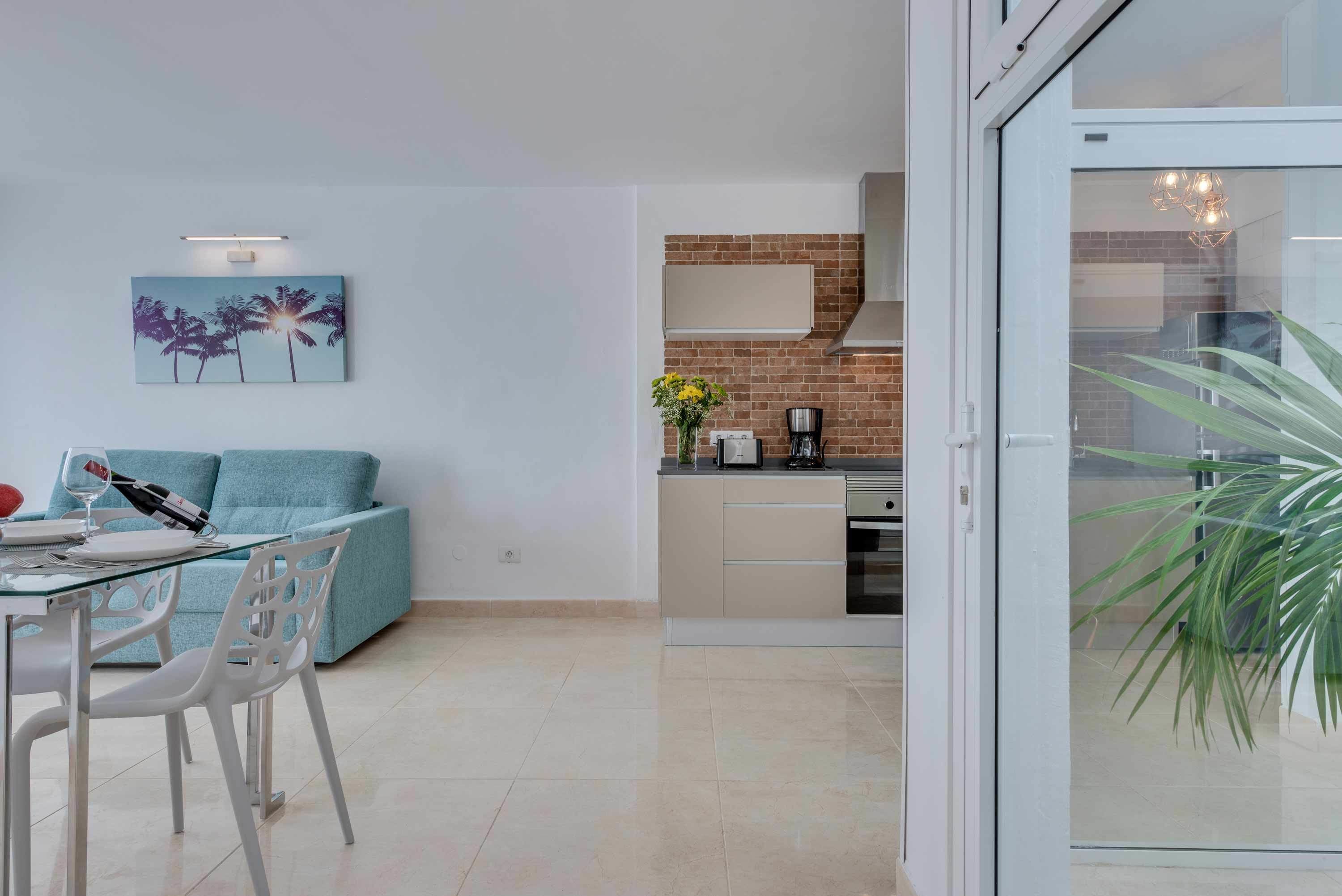 Een moderne woonkamer met een glazen eettafel, een bank en een keuken met een bakstenen achterwand en roestvrijstalen apparatuur.