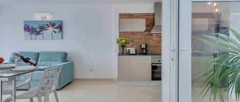 Een moderne woonkamer met een glazen eettafel, een bank en een keuken met een bakstenen achterwand en roestvrijstalen apparatuur.