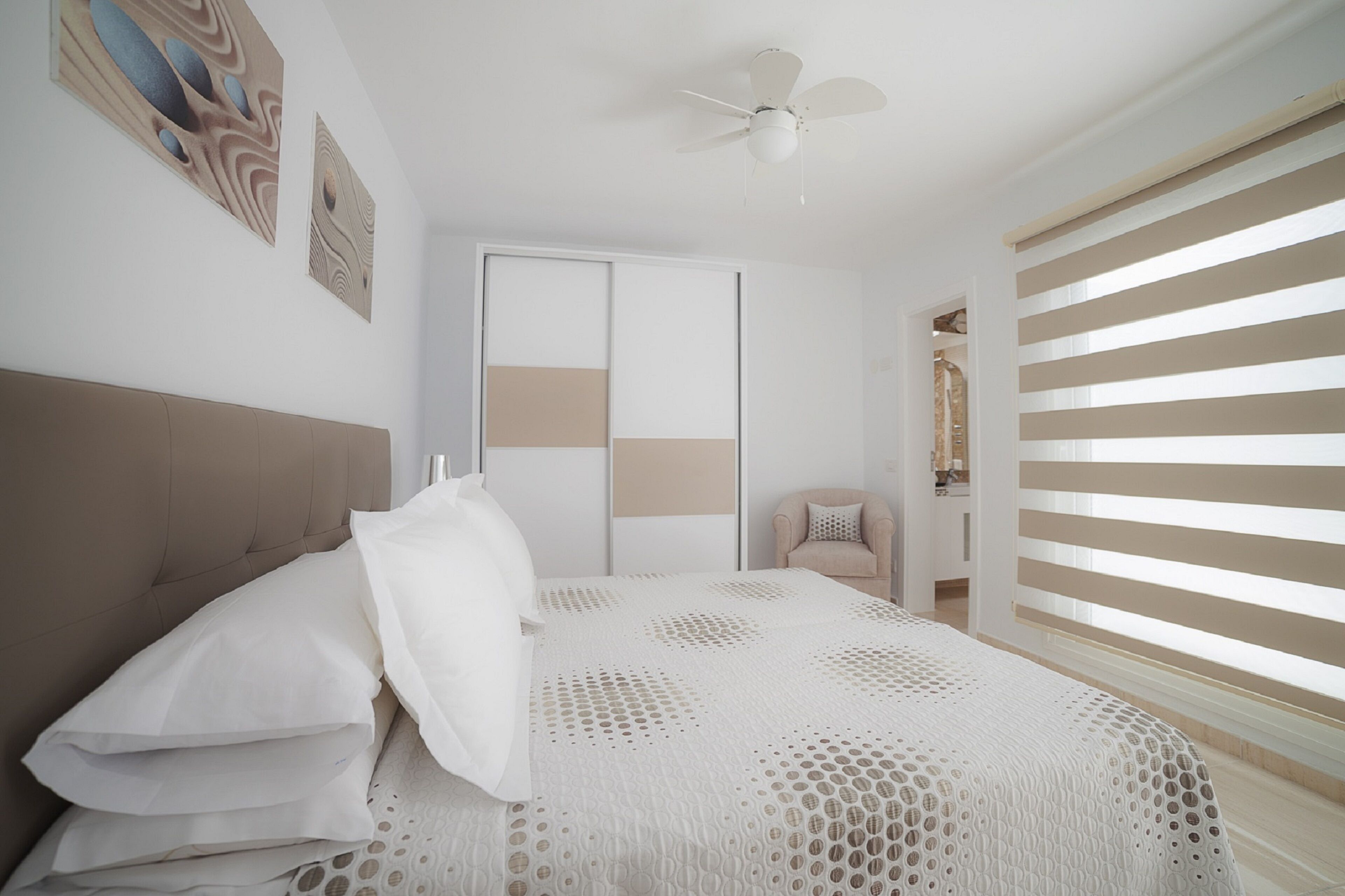 A bedroom with a bed, a ceiling fan, a window with blinds, and a door.