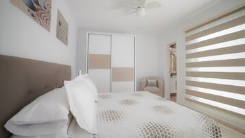 A bedroom with a bed, a ceiling fan, a window with blinds, and a door.