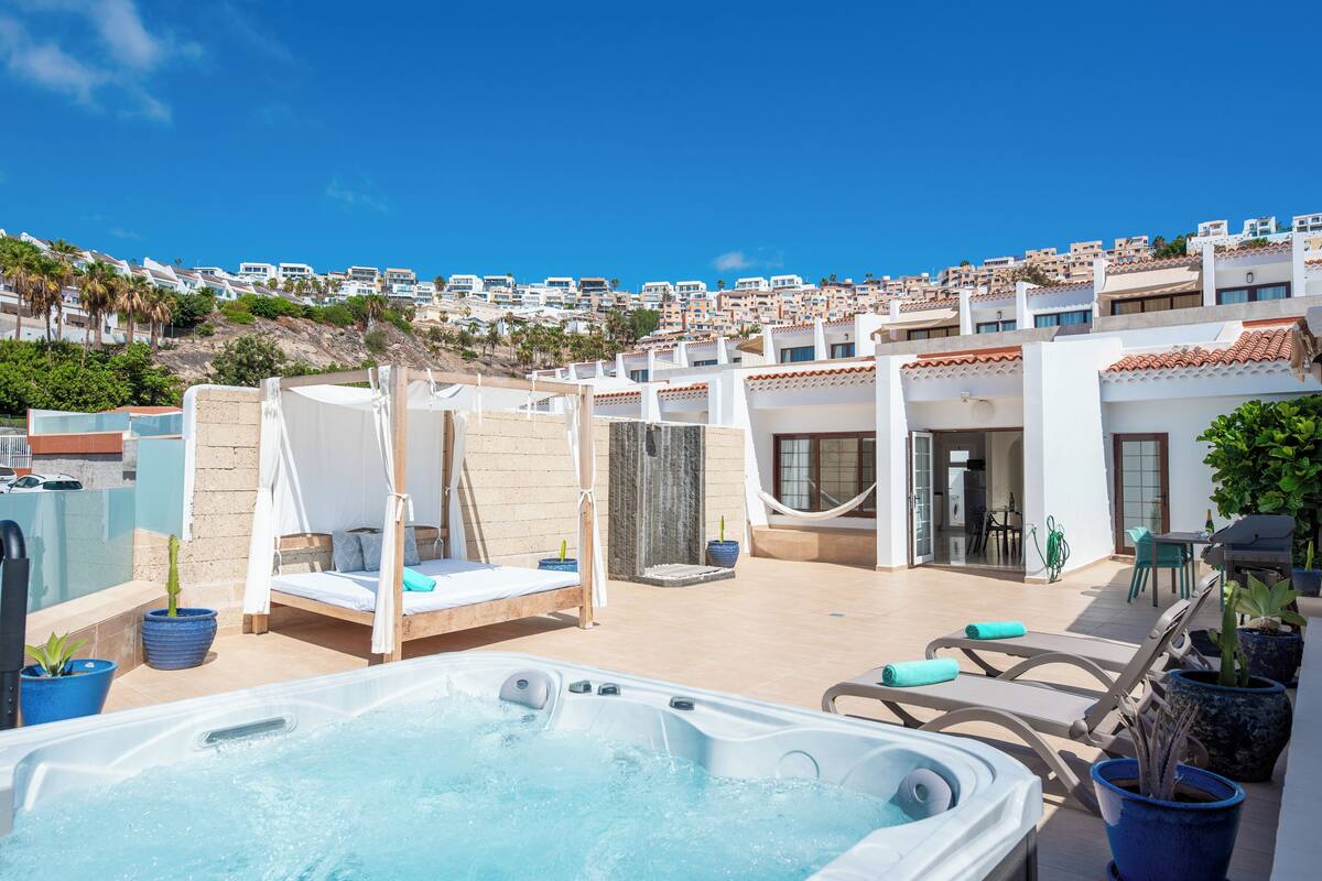 Un área de piscina en la azotea con hidromasaje, sillas de descanso y vistas a una zona residencial en una colina.
