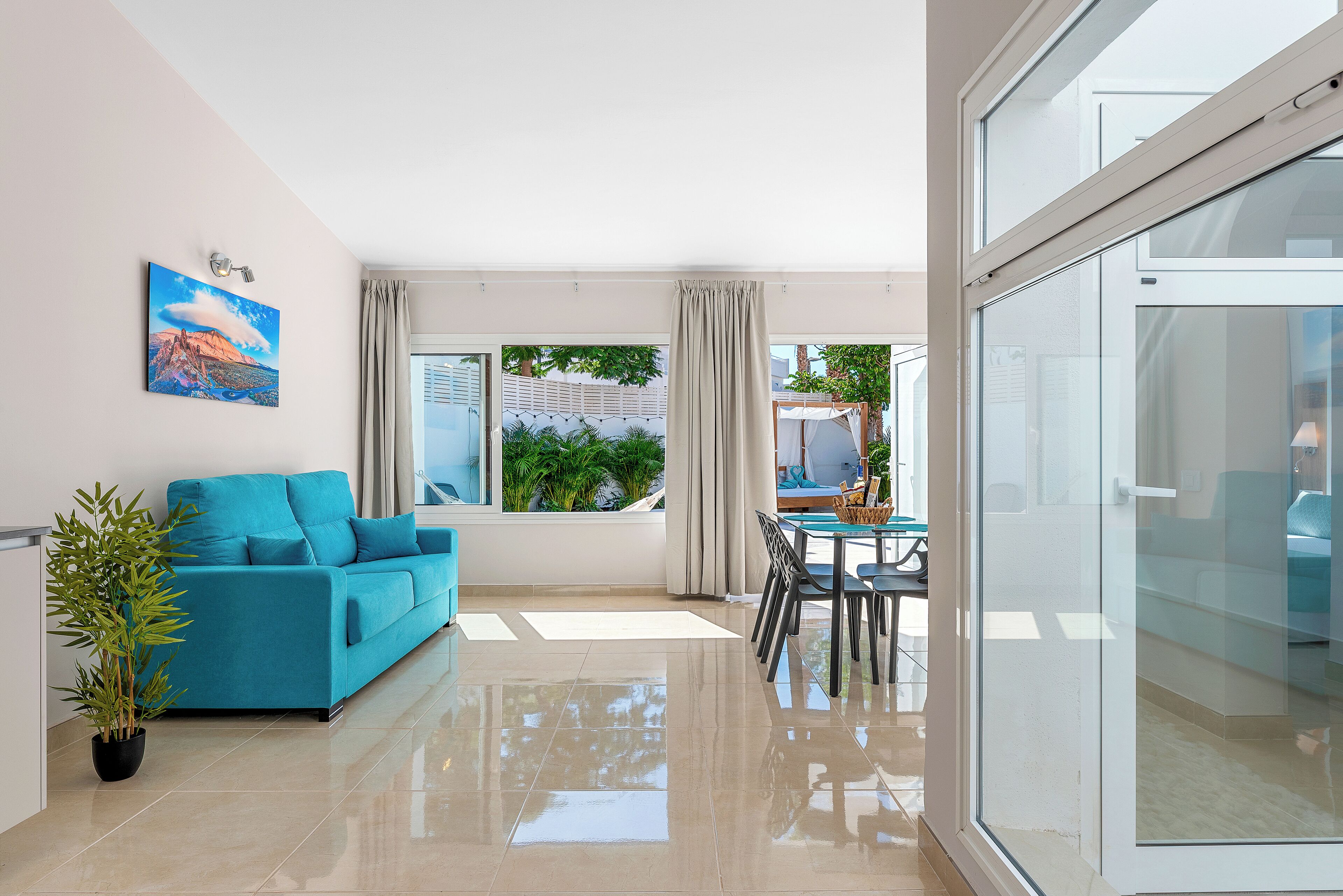 A modern living room with a blue sofa, a potted plant, and a dining area with a table and chairs.