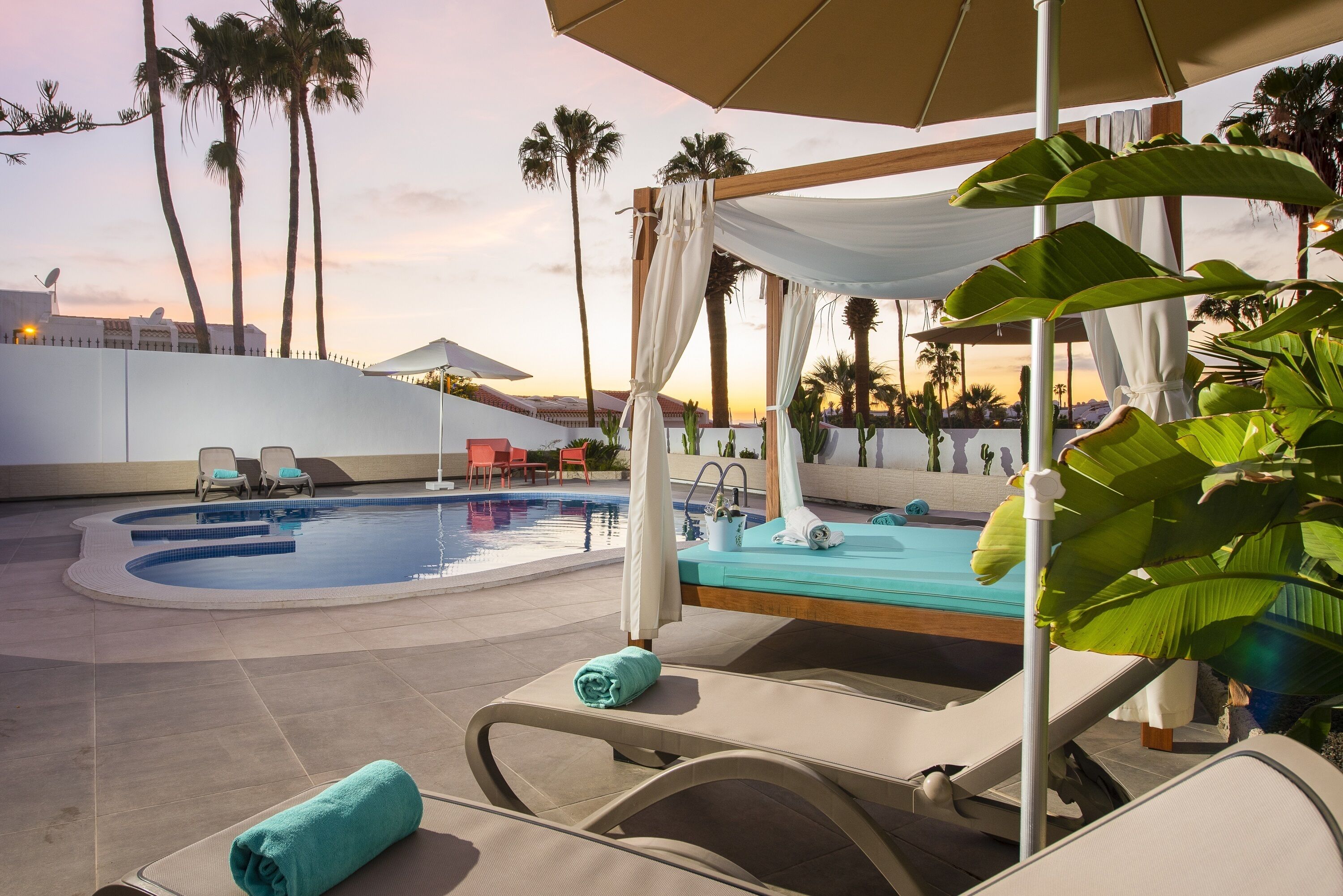 Un área de piscina con sillones de descanso, un jacuzzi y palmeras.