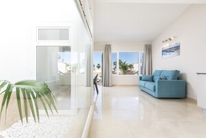 Una sala de estar moderna con un sofá azul, un separador de vidrio y vistas a palmeras y edificios al exterior.