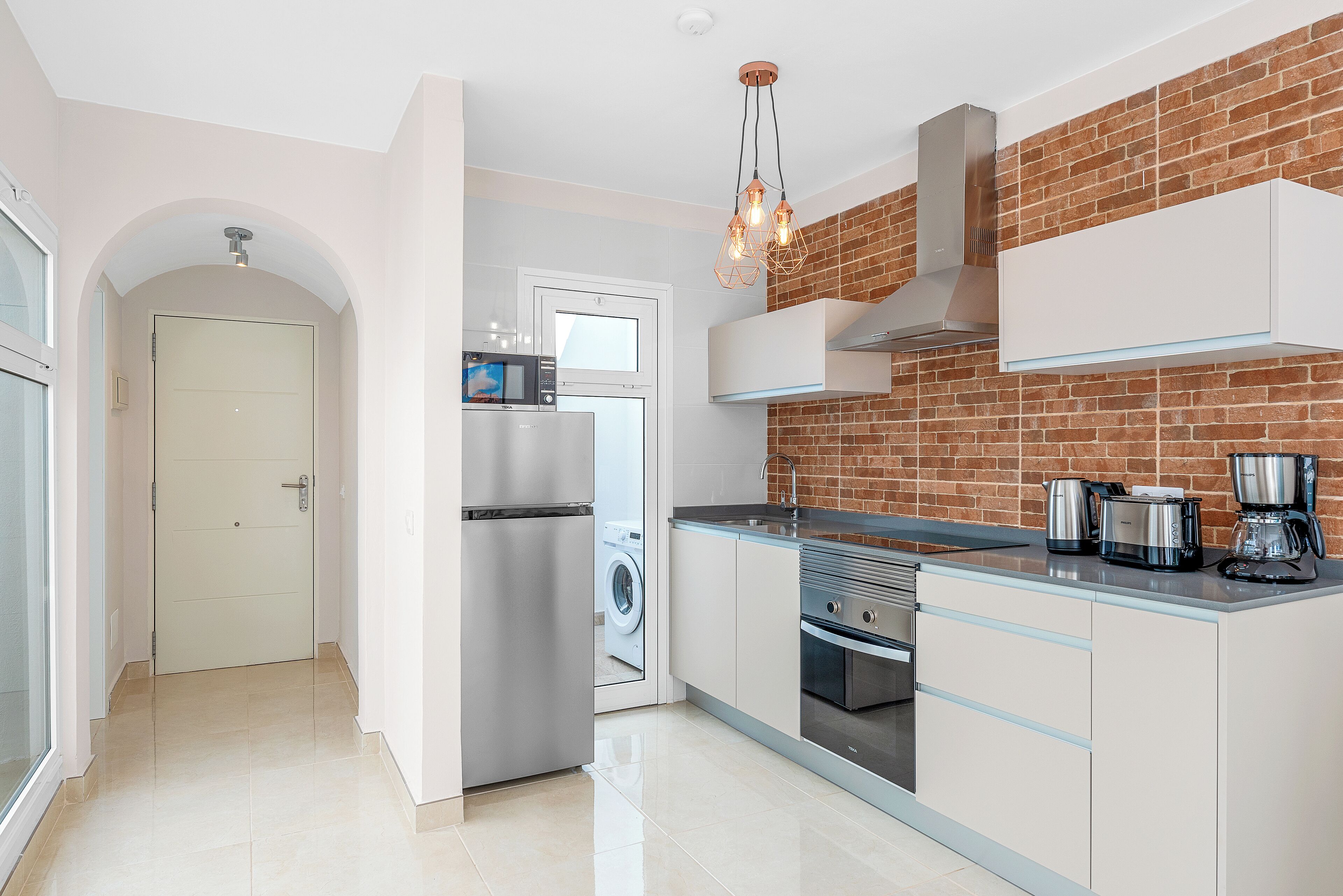 A modern kitchen with stainless steel appliances, a brick accent wall, and a sleek countertop.