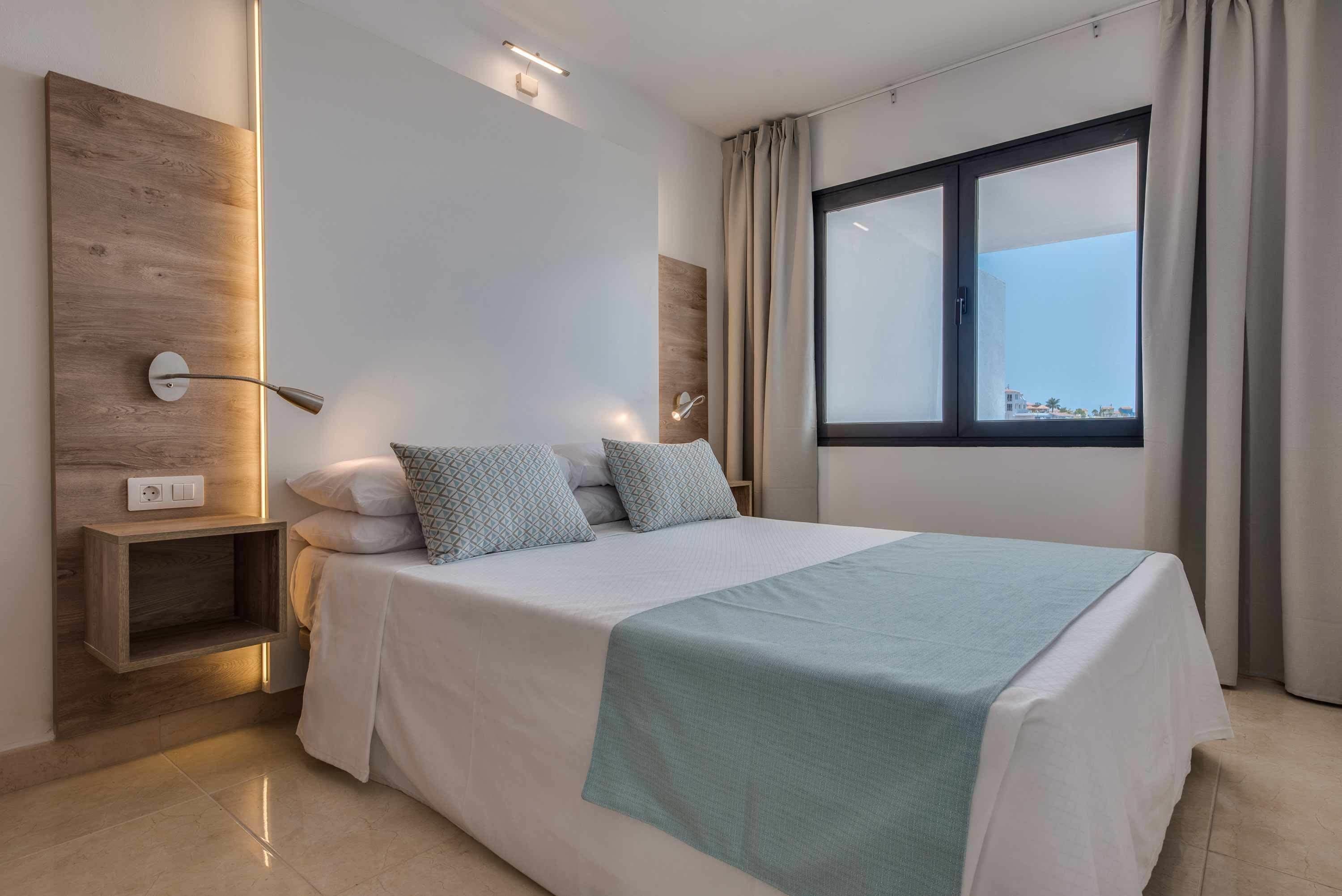 Camera d'albergo moderna con un letto grande, un comodino, una lampada a parete e una finestra con tende.