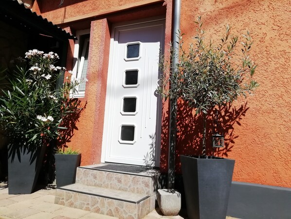Un edificio con una puerta blanca, escalones de piedra y macetas con plantas.