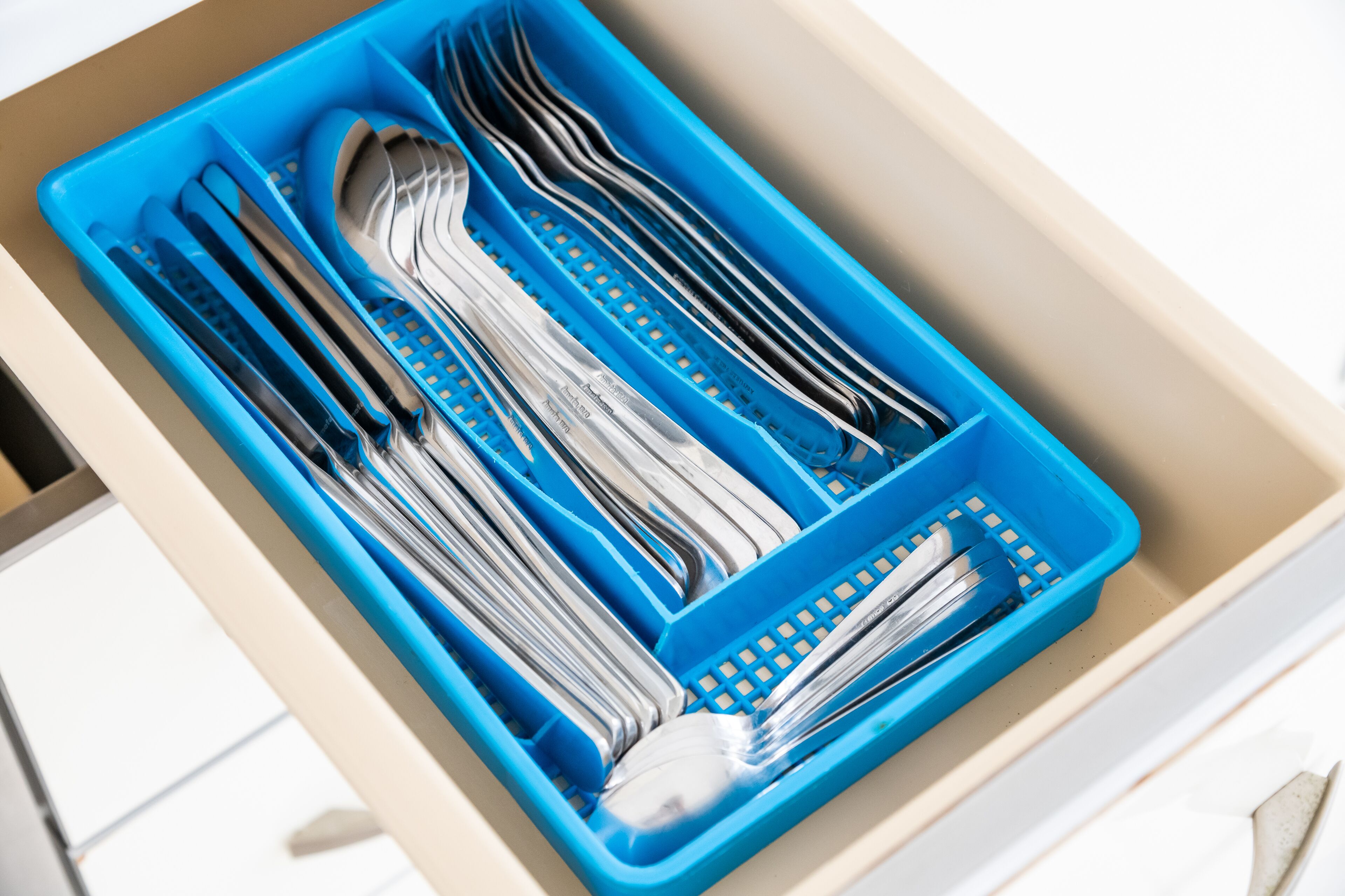 A drawer with a blue utensil organizer containing forks, knives, and spoons.
