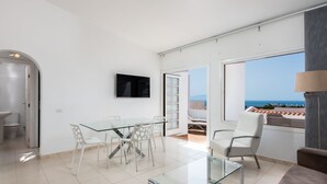 Ein modernes Wohnzimmer mit Glastisch und Stühlen, einem Flachbildfernseher und Meerblick.