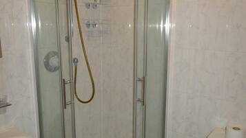 A glass-enclosed shower stall with a handheld showerhead, a toilet, and a sink.