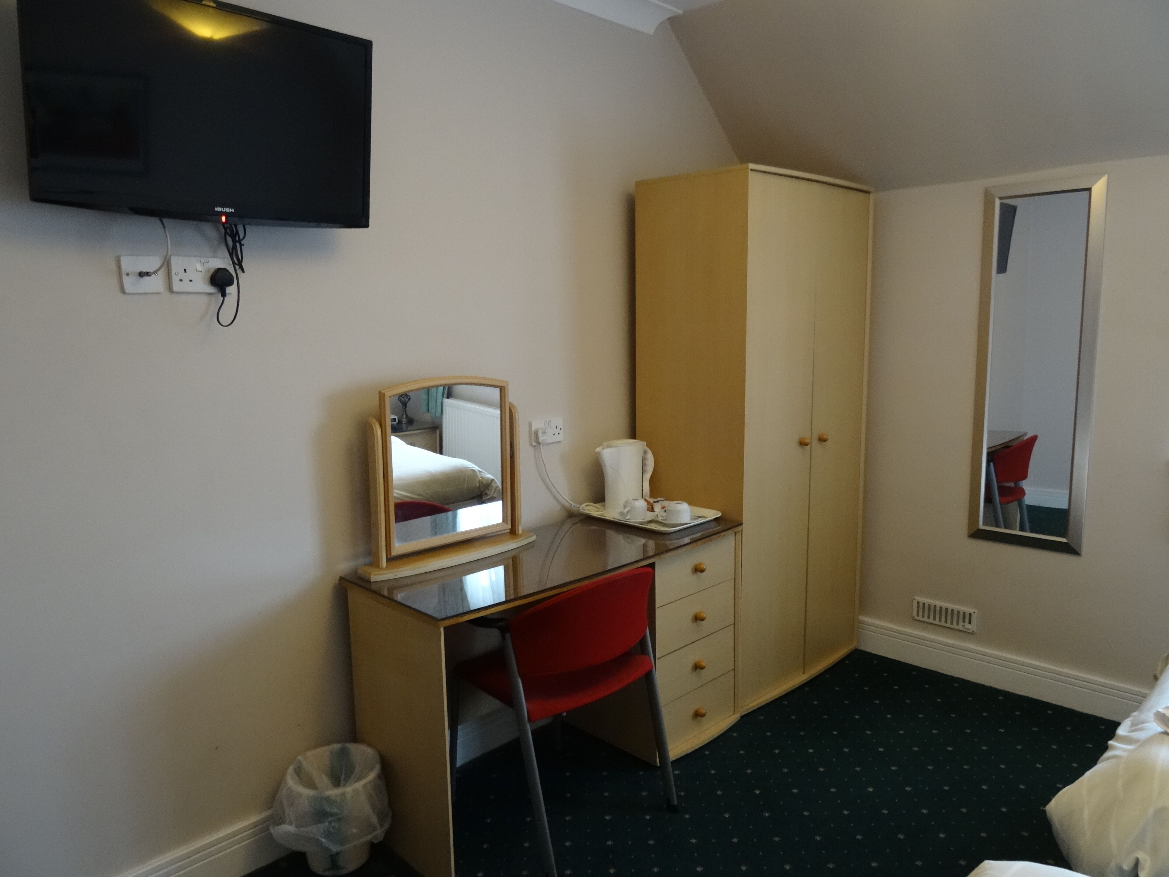 Habitación de hotel con escritorio, una silla, armario, espejo y televisor en la pared.