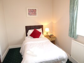 A neatly made bed with white linens and a red pillow, a bedside lamp, a framed picture on the wall, and a window with curtains.