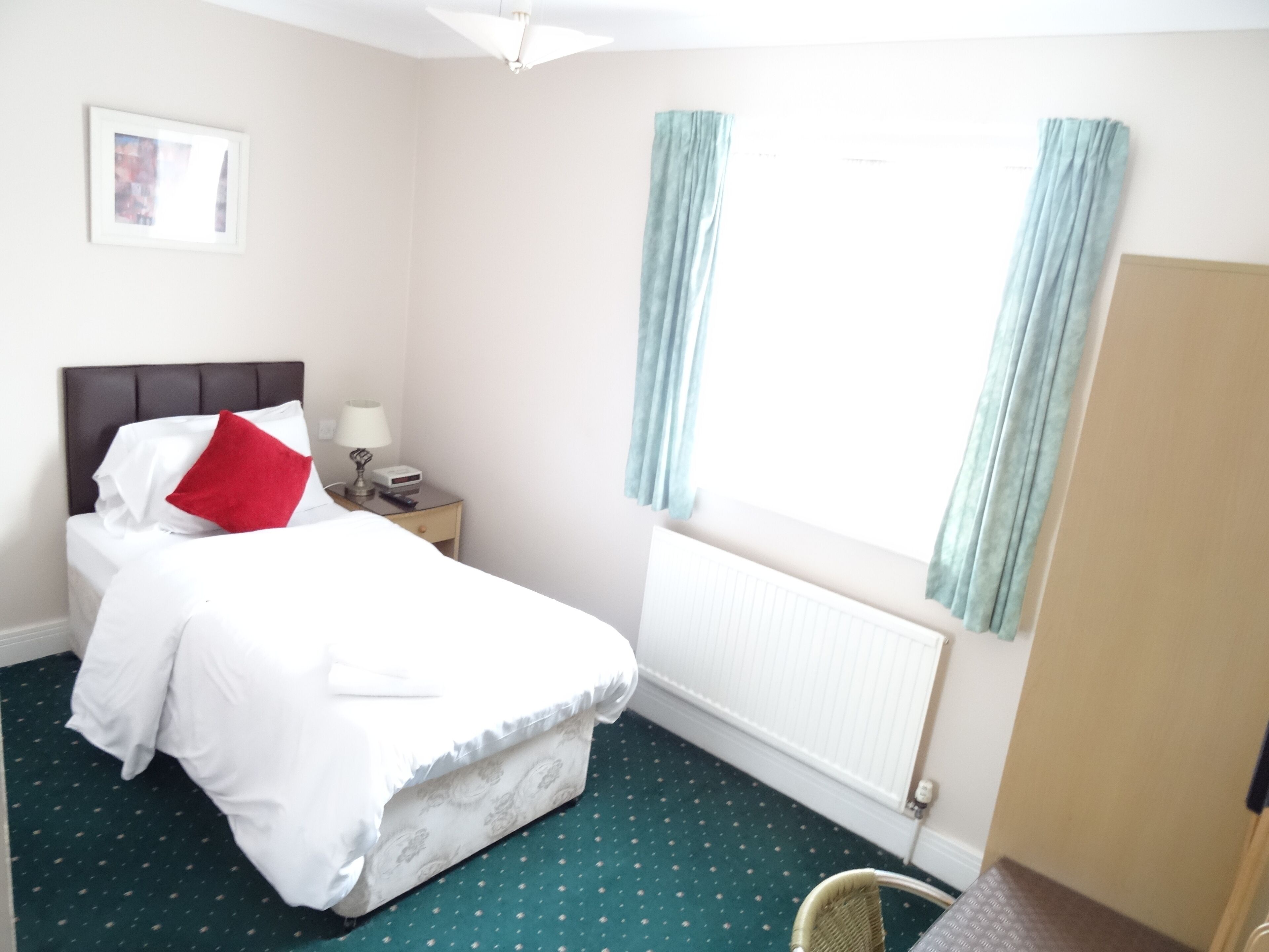 A hotel room with a bed, a nightstand, a lamp, a framed picture on the wall, and a window with curtains.