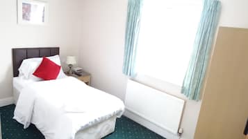 A hotel room with a bed, a nightstand, a lamp, a framed picture on the wall, and a window with curtains.