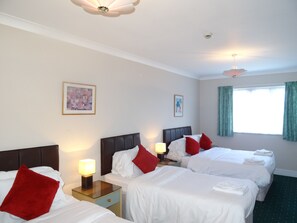 A hotel room with two beds, a nightstand with a lamp, a ceiling fan, and a window with curtains.