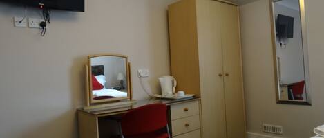 Een hotelkamer met een bureau, een rode stoel, een kledingkast, een bed en een tv aan de muur.
