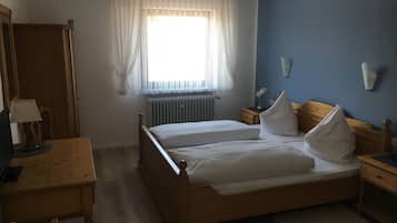 Ein Schlafzimmer mit einem hölzernen Bett, einem Schreibtisch mit Lampe, einem Heizkörper und einem Fenster mit durchsichtigen Vorhängen.