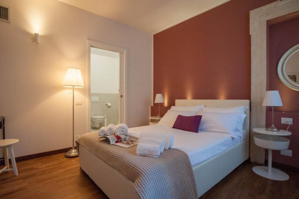 A hotel room with a bed, bedside lamps, a bedside table, a mirror, and a door leading to a bathroom.
