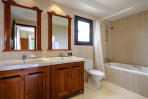 Une salle de bain avec des meubles en bois, un lavabo double, des toilettes et une baignoire.