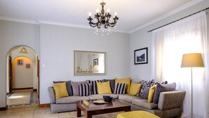 A living room with a sofa set, a coffee table, a yellow ottoman, a floor lamp, a chandelier, a mirror, and a framed picture on the wall. - Villa Anemona (Pegeia)