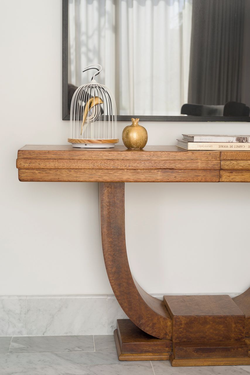 A wooden console table with a curved metal base, a gold spherical object, and a white birdcage with a golden finch.