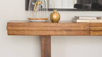 A wooden console table with a curved metal base, a gold spherical object, and a white birdcage with a golden finch.