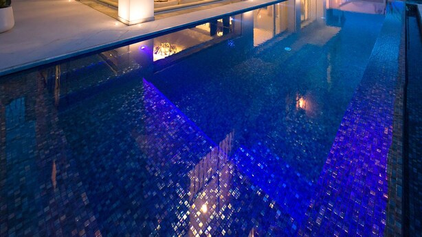 A modern multi-story building with a swimming pool, large windows, and balconies.