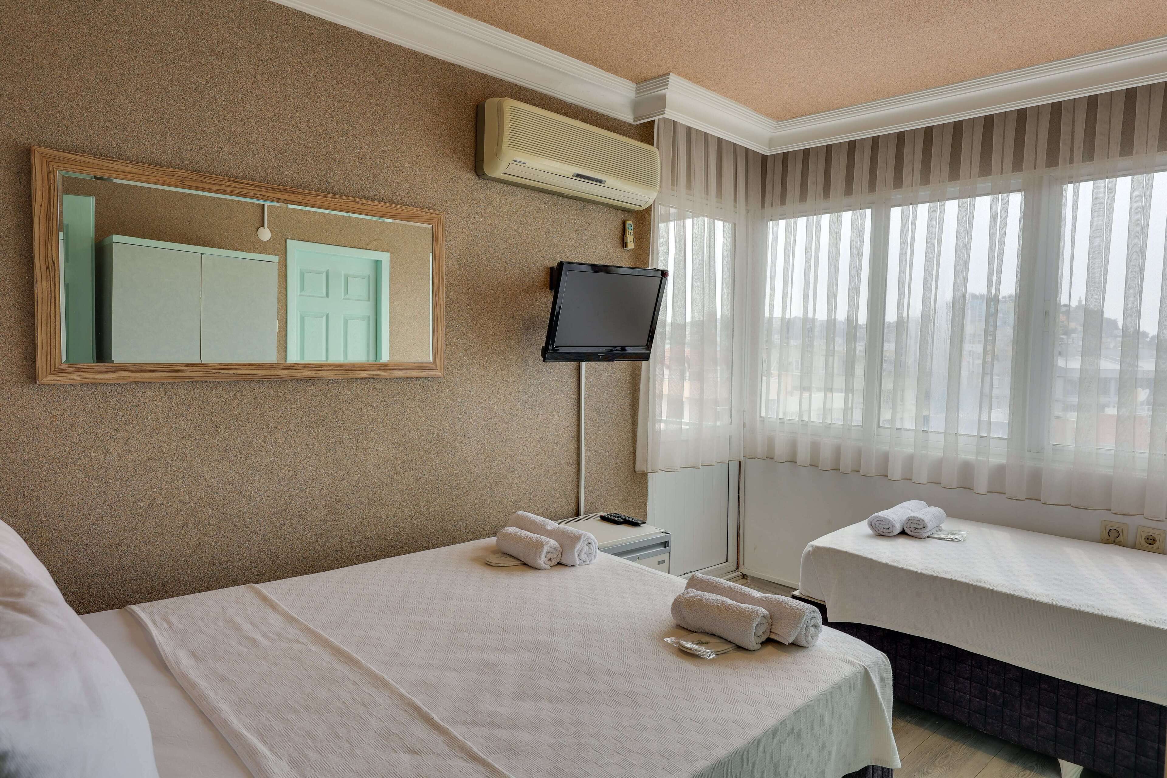 Una camera d'albergo con un letto, una televisione, una finestra con tende e uno specchio sulla parete.