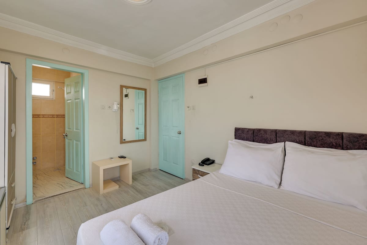 A bedroom with a bed, a bedside table, a nightstand, a mirror, and a door leading to a bathroom.