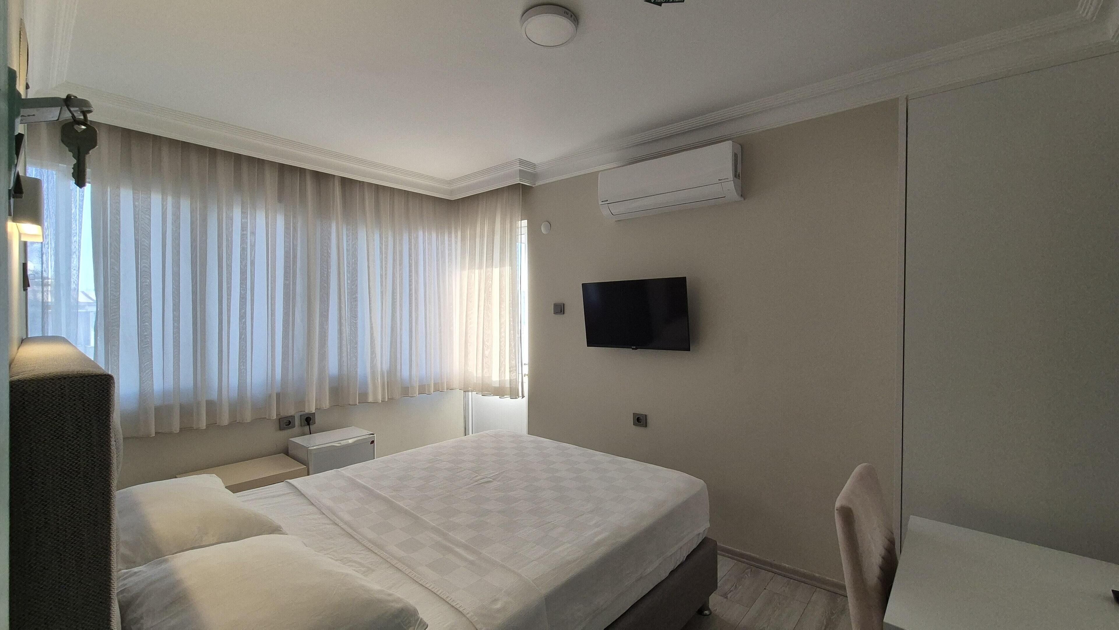 A hotel room with a bed, a TV, an air conditioner, a bedside table, and a chair.