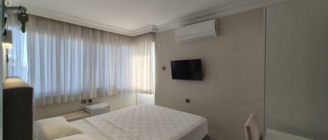 A hotel room with a bed, a TV, an air conditioner, a bedside table, and a chair.