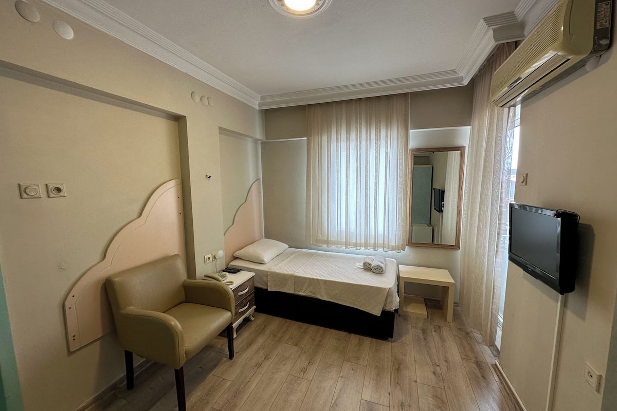 A hotel room with a bed, a chair, a bedside table, a TV, and a window with curtains.