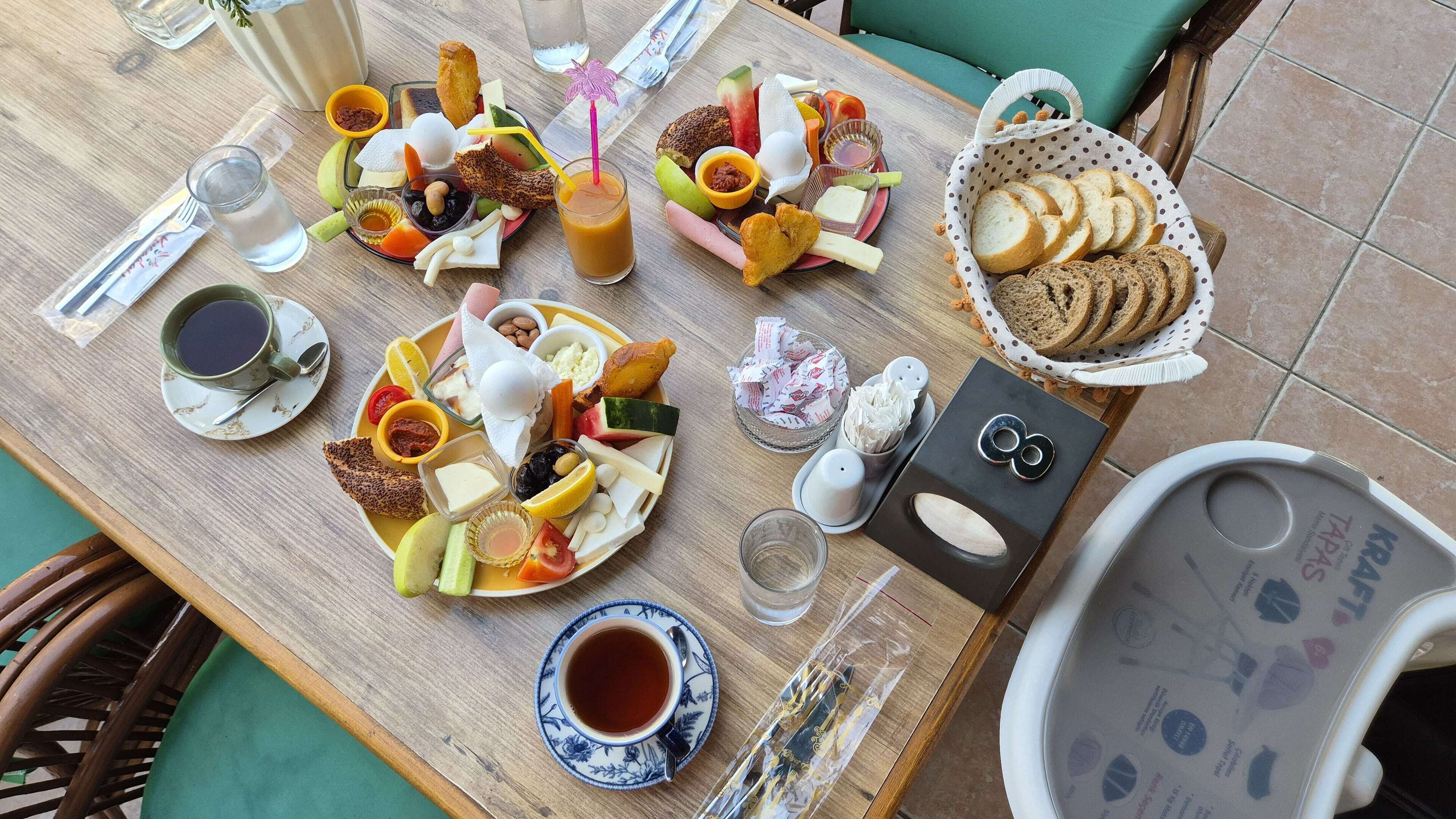 Una mesa de madera con diversos alimentos, como pan, queso y frutas. También hay platos, tazas y una cesta de pan.