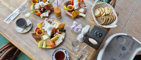 Una mesa de madera con diversos alimentos, como pan, queso y frutas. También hay platos, tazas y una cesta de pan.
